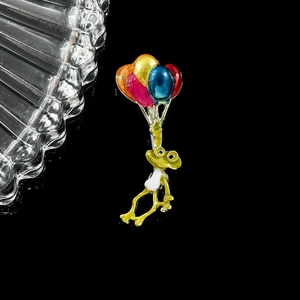 Détail d'un pin's en émail représentant un grenouille verte tenant des ballons colorés