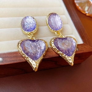 Vintage style gold earrings with purple resin hearts and oval textures on a beige tray