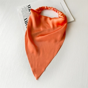 Close-up of orange satin triangle headscarf with elastic band on a magazine background