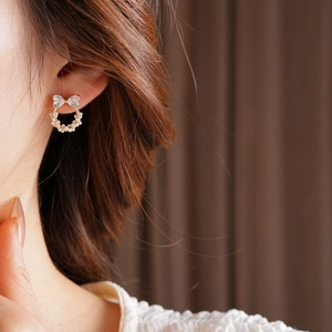 Gros plan d'une puce d'oreille nœud doré avec zircons et petites perles blanches