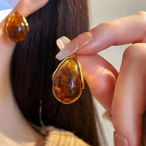Close-up of amber resin teardrop earrings with gold metal base on model's ear