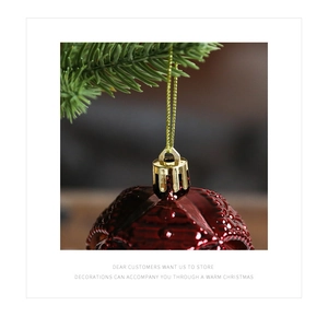 Close-up of deep red textured Christmas ball ornament with golden cap on a pine branch
