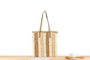 Detail of striped woven paper straw tote bag with brown straps on a wooden table