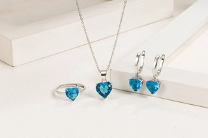 Detail view of silver jewelry set with blue heart-shaped gems, including necklace and ring