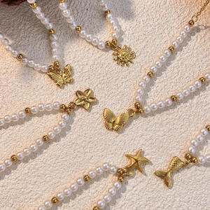 Stainless steel pearl necklace with gold butterfly and sun charms on stone background
