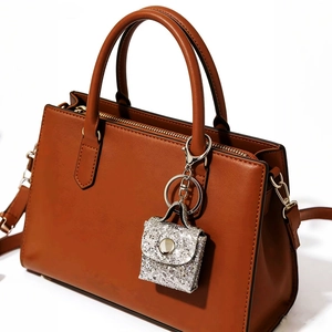 Mini silver glitter handbag keychain charm hanging on a brown leather tote bag