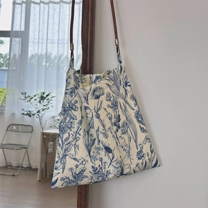 Detail of blue floral print cotton tote bag hanging with slim brown leather strap