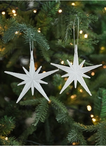 White glittery star ornaments hanging on a Christmas tree with warm light decorations