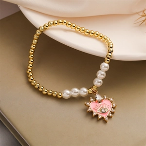Detail of gold beads and pearls bracelet with pink heart evil eye charm on silk