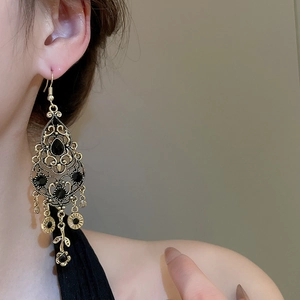Dettaglio di orecchini vintage dorati con nappine e strass neri indossati da una modella