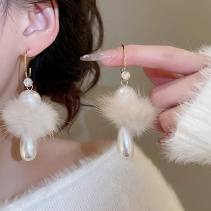 Detailed close-up of a golden C-shaped earring with white pearl and plush pompom detail