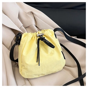 Detailed view of yellow drawstring bucket bag with black strap on a beige trench coat
