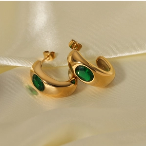 Macro detail of 18K gold plated C-shaped earrings with green zircon on silk fabric