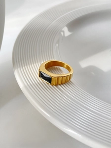 Macro detail of golden stainless steel ring with black rectangular stone and ribbed band