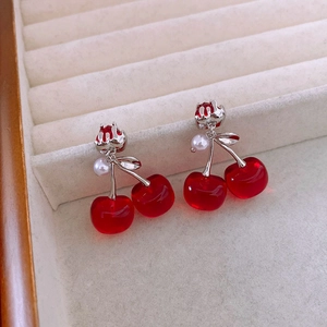 Dettaglio di orecchini a forma di ciliegia con perle rosse traslucide e finiture bianche