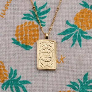 Close-up of golden copper necklace with rectangular sunburst and hexagram star pendant