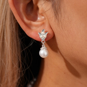 Detailed close-up of leaf-shaped silver earrings with rhinestones and white pearls