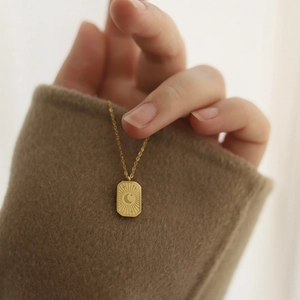 Détail d'un pendentif rectangulaire en or 18K avec lune et étoiles sur un pull marron