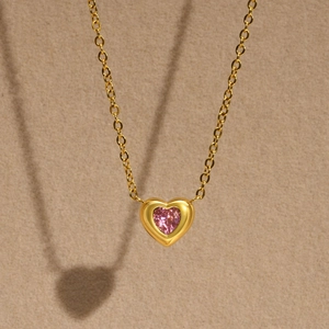 Detailed close-up of 18K gold heart necklace with a sparkling pink zircon gemstone center