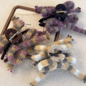 Three knitted bow hair claws in purple, brown, and yellow stripes on a wooden tray