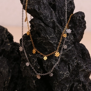 Close-up of 18K gold and silver daisy flower pendants on a textured black rock surface