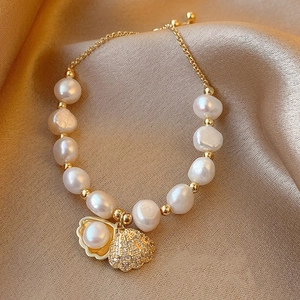 Detailed macro view of baroque pearl bracelet with gold shell charm on silk fabric