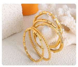 Detail of gold-plated bangle set featuring bamboo texture, pearls and rhinestones on coral
