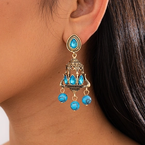 Detailed close-up of Bohemian gold earrings with blue gemstones worn by a model