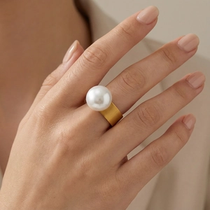 Close-up of a wide gold stainless steel ring featuring a large round white pearl inlay