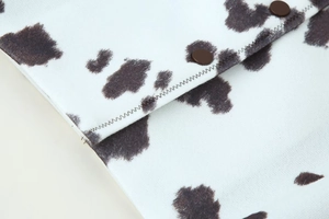 Détail de la veste imprimé vache avec boutons-pression bruns et coutures en zigzag