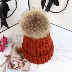 Nahaufnahme der orangefarbenen Strickmütze mit Kunstfell-Bommel neben Geschenktüte