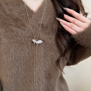 Detailed close-up of a long golden butterfly tassel necklace on a dark plush sweater