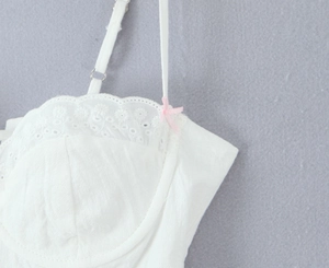Close-up of white lace embroidery detail with a small pink bow on a camisole dress