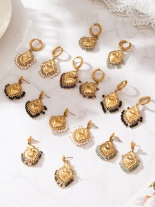 Détail de boucles d'oreilles cœur dorées avec perles colorées sur marbre blanc