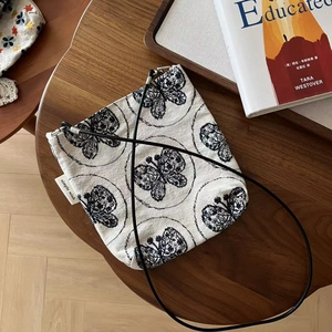 Petit sac en toile brodé vintage avec motif papillon posé sur une table en bois naturel