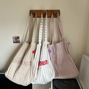 Three striped canvas tote bags in beige, white, and pink hanging on a wooden rack