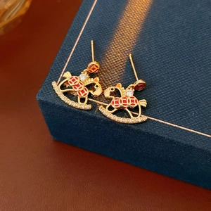 Close-up of gold rocking horse earrings with red enamel and inlaid clear gemstones