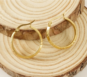 Macro shot of 18K gold plated hoop earrings with Greek key pattern on wooden texture