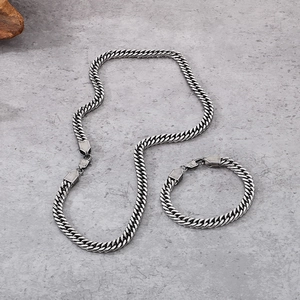 Detailed top view of vintage silver Cuban link necklace and bracelet set on stone texture