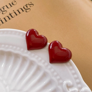 Close-up of red heart earrings displayed on a white vintage plate with books