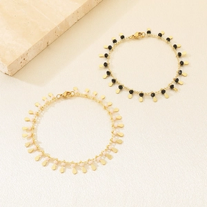 Detail of gold bracelets with black and pink beads and water drop charms on fabric