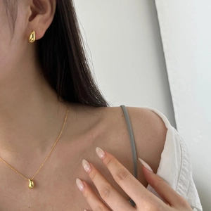 Close-up of minimalist golden teardrop necklace and matching earrings set on model