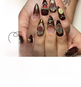 Detailed view of dark red almond nails with 3D embossed gold crosses and heart gems