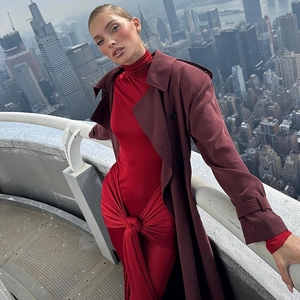 Robe mi-longue rouge avec nœud à la taille et trench-coat bordeaux sur fond de ville