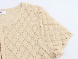 Detailed macro view of the light beige hollow knit pattern and button-up front on the cardigan
