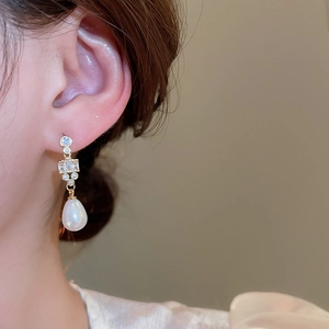 Detailed shot of gold plated drop earrings with white pearl and sparkling zircons