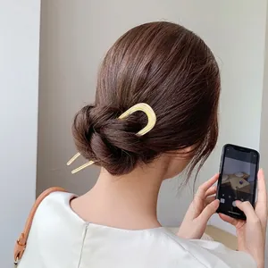 Detail view of a gold-toned U-shaped metal hair fork styling a sleek French hair bun