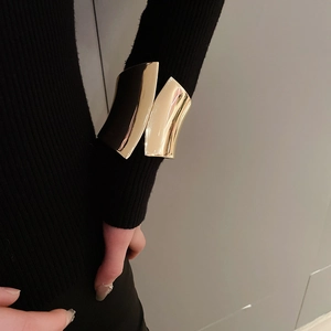 Detail of wide irregular gold cuff bracelet worn over black sleeve with high-shine finish