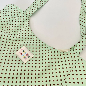 Close-up of green canvas tote bag with brown polka dots and a white branded fabric label