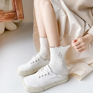 Cream crew socks with ruffled cuffs and flower embroidery paired with white shoes